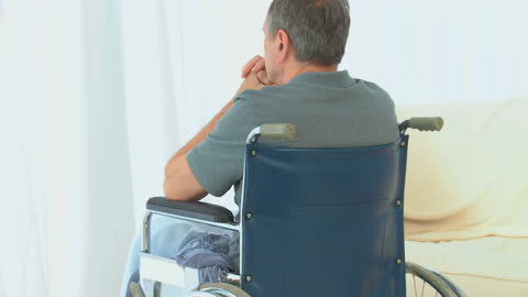 Thoughtful Man in Wheelchair Gazing Out Window at Home
