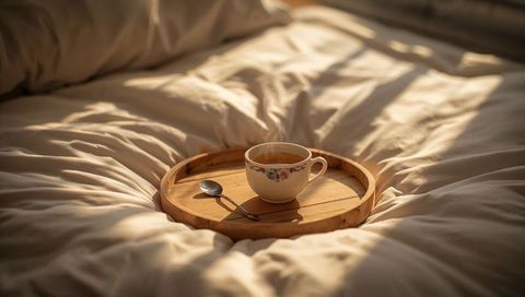 Sunlit tea on wooden tray resting on cream duvet, cozy morning breakfast in bed
