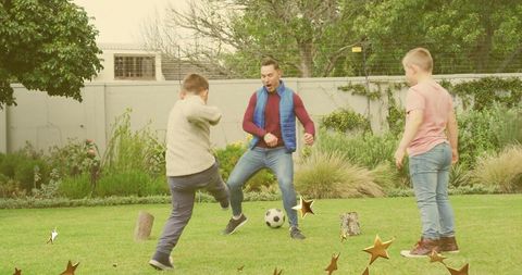 Backyard soccer match with father and two boys kicking ball around wooden stumps