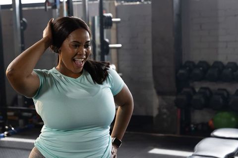 Confident african american woman smiling and posing in gym with dumbbells and kettlebells