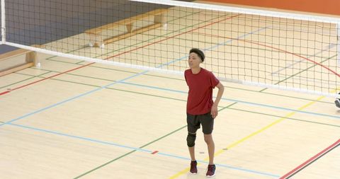 Teen african american volleyball player standing under net on indoor sports court
