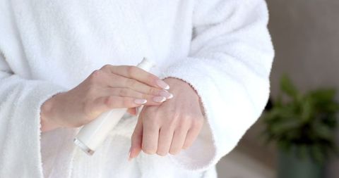 Woman Using Lotion in White Bathrobe for Skincare and Relaxation