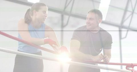 Woman wrapping hands while coach coaching in boxing ring with skylight flare