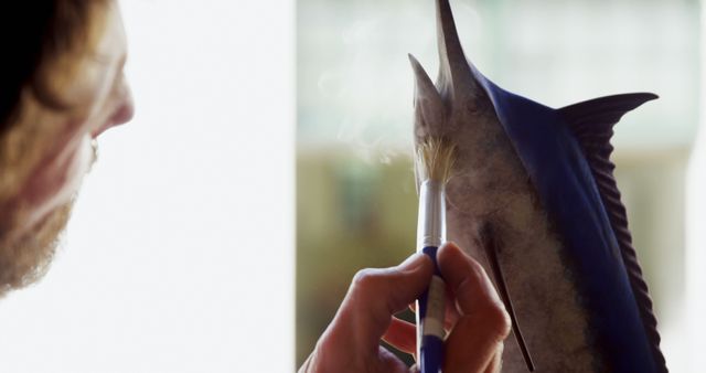 Man interacting with swordfish beak using paintbrush, highlighting focus on marine life and detailed craftsmanship. Ideal for illustrating detailed marine wildlife studies, artistic activities, or the human connection with nature.