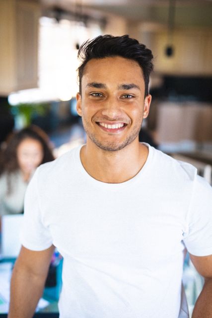 Young biracial man smiling confidently while standing at home. Ideal for use in lifestyle, happiness, and diversity-related content. Perfect for promoting positive emotions, casual fashion, or home environments.