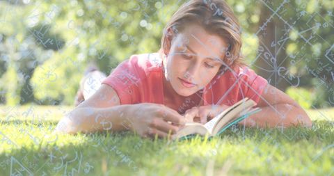 Focused Young Woman Reading Book on Sunny Grass