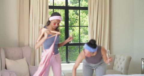 Diverse friends in loungewear enjoying champagne while arranging satin dress and cozy bed