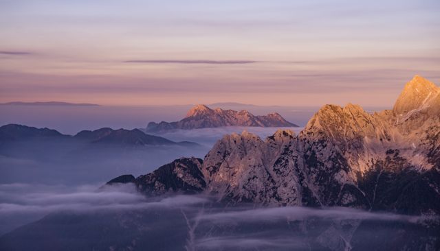 Mountain range at twilight with low clouds creates serene and majestic view, perfect for nature photography, travel blogs, environmental projects, and meditation materials. Soft light and tranquil sky make it ideal for backgrounds and desktop wallpapers.