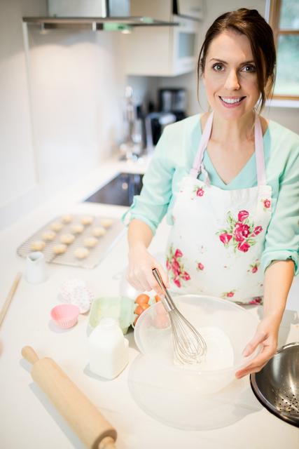 Portrait of beautiful woman whisking flour in bowl at kitchen