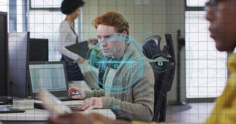 Redhead developer typing on laptop with cybersecurity hologram overlay in open office