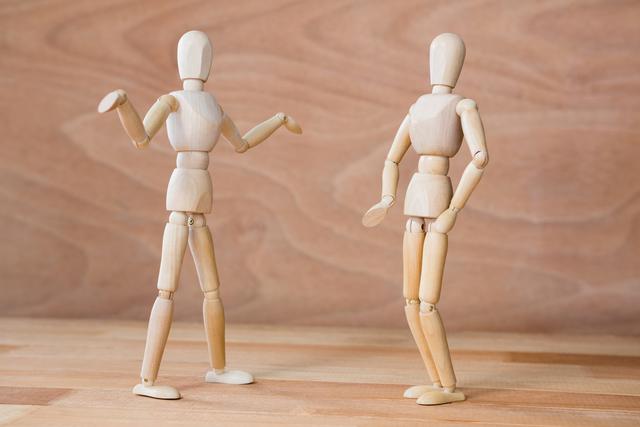Two wooden mannequins are engaged in an argument, with one gesturing animatedly while the other stands with a defensive posture. This image can be used to illustrate concepts of conflict, communication, and relationships. It is suitable for articles, blogs, and educational materials discussing interpersonal dynamics, body language, and conflict resolution.