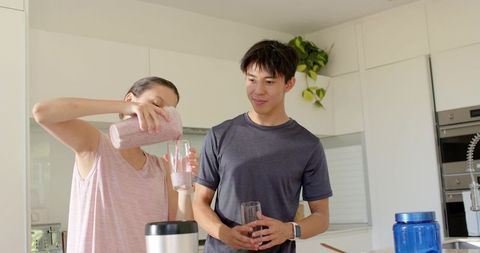 African american woman and asian man preparing pink smoothie in modern white kitchen