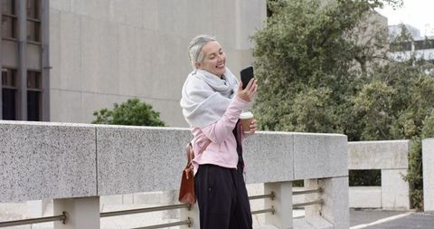 Mature woman enjoying coffee while chatting on smartphone on urban terrace