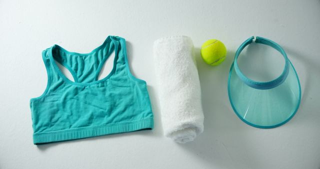 Various women's fitness items including a turquoise sports bra, white towel, tennis ball, and turquoise visor arranged on a white background. Useful for illustrating fitness routines, promoting sportswear brands, highlighting workout essentials, or depicting healthy lifestyle themes.