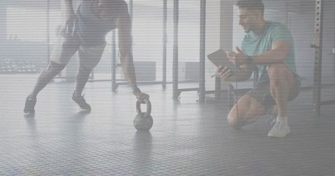 Personal trainer coaching kettlebell lunge near windows on rubber gym floor for strength