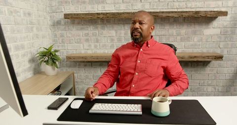 Focused man in red shirt working at desk with computer and coffee