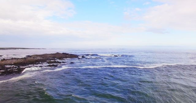 Peaceful view of a calm ocean with gentle waves hitting a rocky shore under an expansive sky. Ideal for backgrounds, relaxation themes, travel brochures, coastal nature blogs, and meditation apps.
