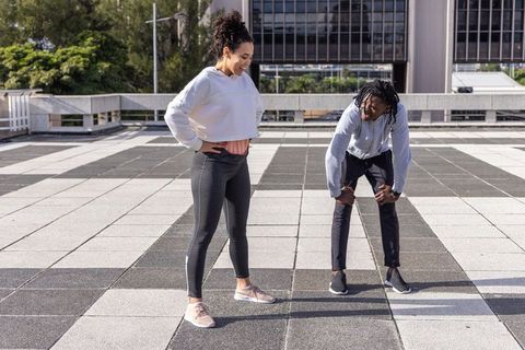 Urban rooftop fitness duo pausing and laughing during outdoor workout in activewear