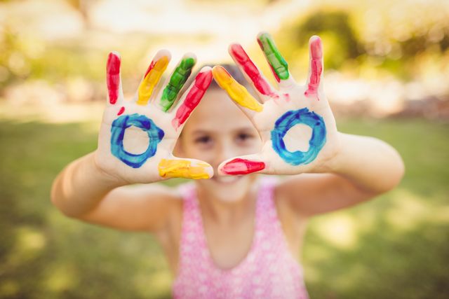 Child with colorful painted hands enjoying outdoor activity in park. Perfect for themes related to childhood, creativity, fun, and outdoor play. Ideal for educational materials, parenting blogs, and advertisements promoting children's activities.