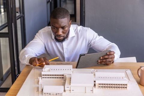 Architect analyzing model with tablet in modern office