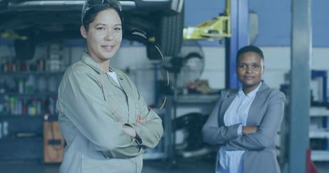 Woman mechanic standing with arms crossed while manager in blazer watching by vehicle lift