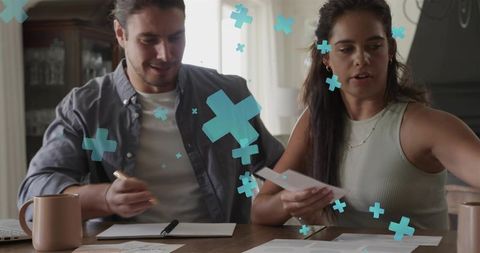 Young couple reviewing finances at home with turquoise plus icons for budgeting