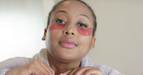 African american woman wearing red under-eye patches and false lashes adjusting bathrobe