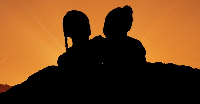 Silhouette of two children against a vivid orange sunset sky, capturing a moment of bonding and togetherness. Ideal for use in content related to childhood memories, family, friendship, and nature. Suitable for educational materials, blog articles, and inspirational posts focusing on emotional connections and the beauty of outdoor moments during twilight hours.
