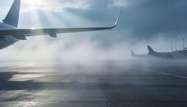 Glinting jet wing with winglet over foggy wet tarmac at dawn sunrays breaking through