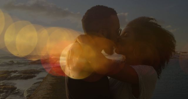 Image of lens flares over diverse couple kissing and hugging on beach against sea and sky. Digital composite, multiple exposure, love, togetherness, happiness, vacation and romance concept.