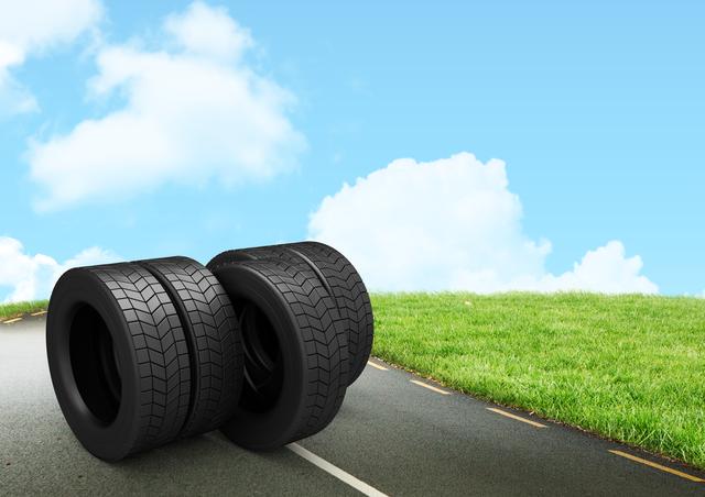 This image shows a stack of tires placed on a road with a clear blue sky and green grass in the background. It can be used for automotive advertisements, transportation services, tire sales promotions, or travel-related content. The bright and clear setting conveys a sense of readiness and reliability.