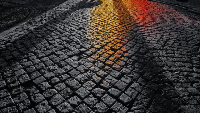 Wet cobblestone street reflecting orange-red neon glow at night, moody urban texture
