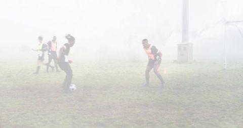 Soccer players practicing dribbling and defending in heavy fog on outdoor training pitch