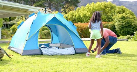 Father and Daughter Setting Up Blue Tent in Green Backyard