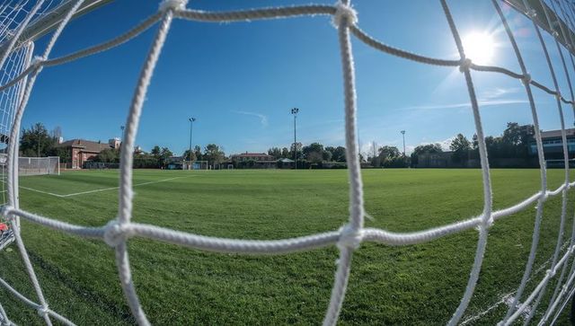 Framing white knotted soccer net in foreground overlooking sunlit green soccer pitch