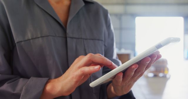 Close-up image of a professional operating a digital tablet within a warehouse environment. Showcasing the use of modern technology in industrial or logistics settings. Perfect for content related to technology integration in warehouse management, efficiency improvements, industrial work processes, and modern business solutions.