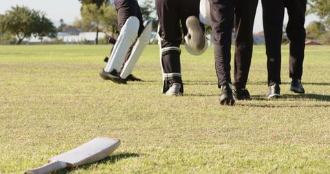Diverse cricket team walking off field celebrating high-five after match victory