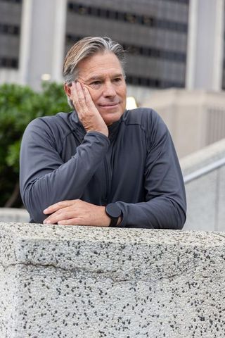 Contemplative senior man leaning on concrete ledge in urban plaza wearing smartwatch