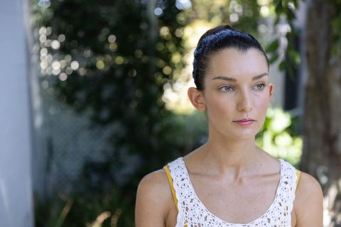 Serene young woman looking right in sunlit garden wearing crochet top with yellow strap