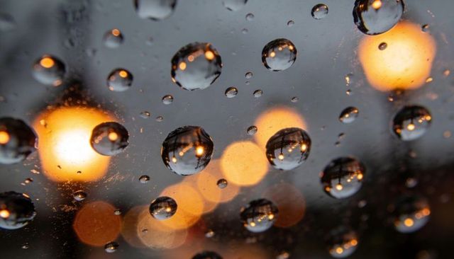 Raindrops on glass reflecting warm bokeh street lights at dusk urban rainy night macro
