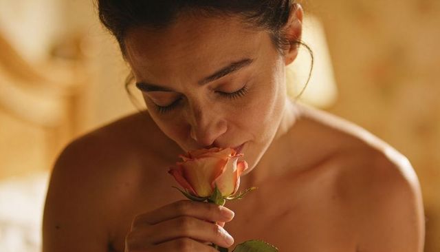 Woman inhaling scent of peach rose closeup intimate boudoir warm golden light