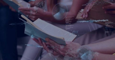 Hands holding paperback book during group reading with digital data overlays