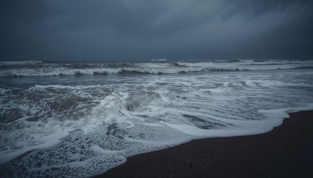 Moody stormy seascape with rolling foamy waves over dark sand shoreline at dusk