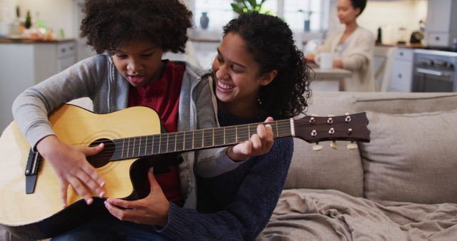 Mother Teaching Son to Play Guitar While Family Relaxes at Home - Download Free Stock Images Pikwizard.com