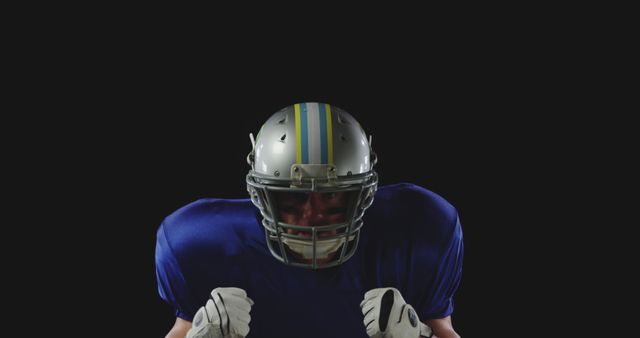 Football player stands determined in complete gear including helmet and blue jersey against dark background. The image is perfect for sports themed content, articles promoting football, athletic determination, and competitive spirit related materials.