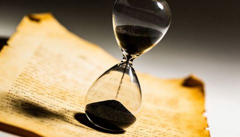 Hourglass pouring black sand over aged parchment manuscript conveying time and history