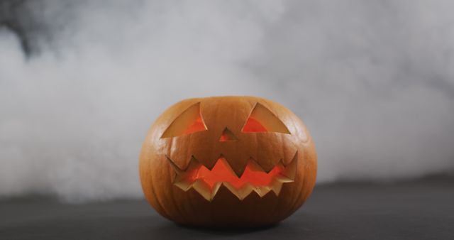 Smoke effect over scary face carved halloween pumpkin against grey background. halloween holiday and celebration concept