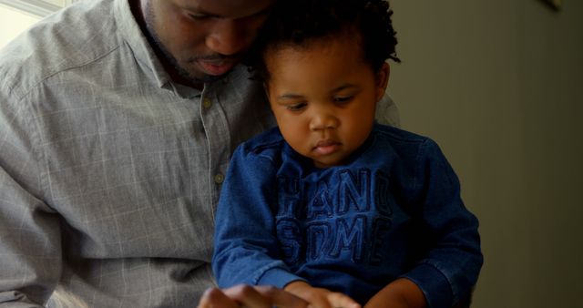 Image showing father and young son sitting together while using a digital tablet. Can be used in articles and materials focusing on family bonding, fatherhood, parenting, education, and the integration of technology in learning.