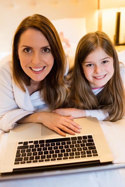 Mother and daughter lying on bed using laptop. The image conveys family bonding and modern technology use. Perfect for blogs, family-oriented websites, technology ads, and home lifestyle themes.