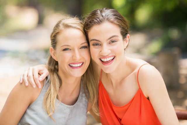 Two women are hugging and smiling outdoors, enjoying a sunny day. They are dressed in casual summer clothes, indicating a relaxed and joyful moment. This image can be used for promoting friendship, outdoor activities, lifestyle blogs, or advertisements focusing on happiness and togetherness.
